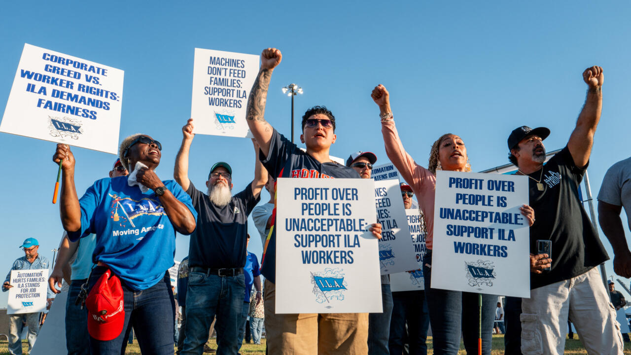 Dockworkers walking a picket line near idle container cranes during a U.S. port strike